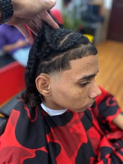 Side profile in the chair: cornrows on top over a fade, with a crisp line-up at the temple.